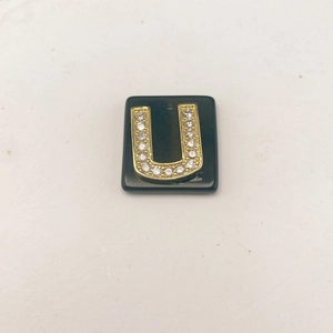Makroansicht des schwarzen quadratischen Anhängers mit goldenem Kristall-Buchstaben U