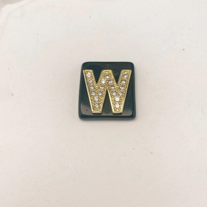 Nahaufnahme des schwarzen quadratischen Anhängers mit goldenem Buchstaben W und Kristallen