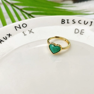 Dettaglio di una pietra a cuore verde smeraldo su una fascia ad anello dorata regolabile