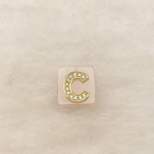 Detailaufnahme eines goldenen Buchstabe C Anhängers mit Zirkonia auf weißem Kunstfell