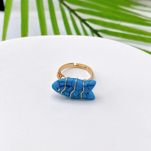 Macro detail of a fish-shaped turquoise ring with wire-wrapped gold band and rhinestone eye