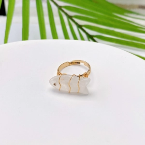 Macro detail of fish-shaped natural white stone ring with wire-wrapped gold metal band