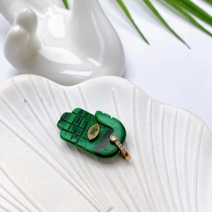 Detail eines grünen Malachit-Hamsa-Anhängers mit Goldakzenten auf einer Schale