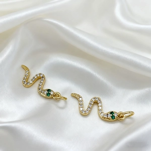 Detailed close-up of gold snake pendant with white zircon and green gemstone eyes