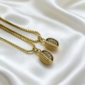 Detail view of two gold coffee bean pendant necklaces with sparkling zircon stones on white silk