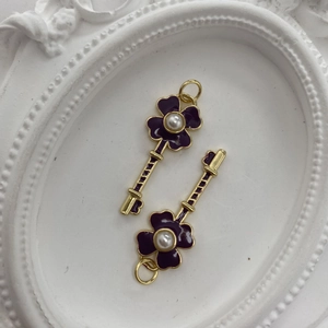 Close-up of golden key-shaped pendants with purple enamel flower and pearl inlays
