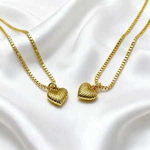 Two 18K gold plated puffy heart pendants with radial texture on a silk fabric background