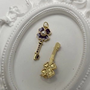 Macro shot of gold key pendant with purple clover enamel and pearl detail for necklace