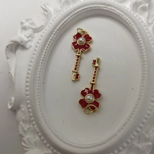 Macro detail of gold flower key pendants with red enamel finish and center pearl inlay