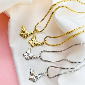 Macro detail of gold and silver butterfly pendant necklaces on elegant white silk background