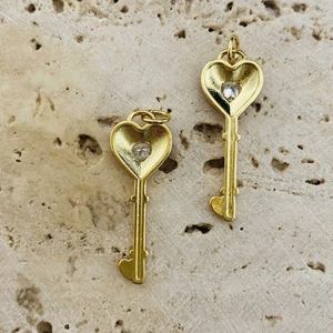 Close-up of gold heart key pendants with sparkling zircon stone on a stone background