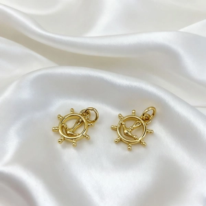 Detailed close-up of 18K gold-plated ship wheel and anchor pendants on white silk
