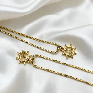 Detail of 18K gold-plated box chain necklaces with anchor and ship wheel charms on silk