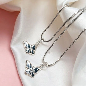 Detailed close-up of two silver butterfly pendants on box chains over pink silk fabric
