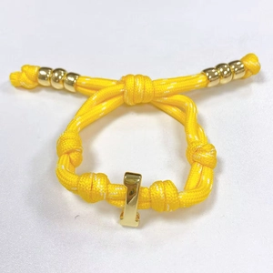 Detailaufnahme des leuchtend gelben geflochtenen Armbands mit goldenen Metallelementen