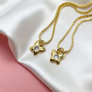 Macro detail of two golden butterfly necklaces with round cubic zirconia on box chains