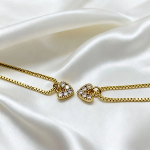 Close-up of gold-plated heart pendant necklaces with crystals on white silk background
