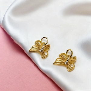 Detail of two gold butterfly charms with hollow texture and zircons on silk fabric