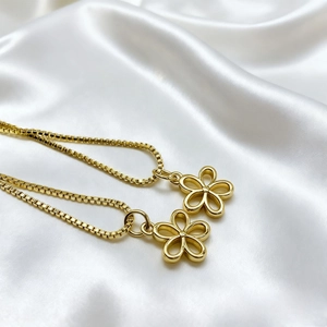 Detail of two 18K gold plated hollow flower pendants on elegant box chains and silk cloth