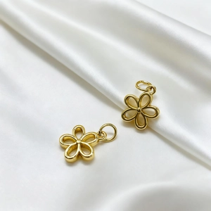 Close-up of golden hollowed-out flower pendants on white silk background for jewelry DIY