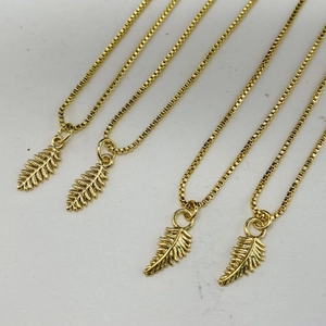 Close-up of four gold leaf pendant necklaces with square link chains on a grey background