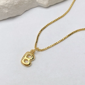 Detalle del colgante de letra B dorada estilo burbuja con una cadena de collar clásica