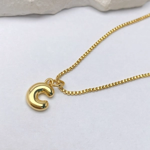 Detalle del colgante de letra C dorada con burbuja en una cadena de caja elegante