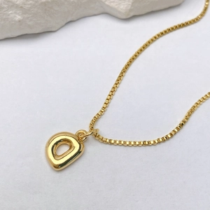 Detalle de un colgante de letra D chapado en oro de 18 quilates con cadena de caja elegante