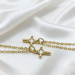 Close-up of dual gold cross necklaces with zircon inlays on white satin fabric