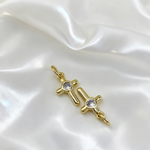 Detail of 18K gold-plated cross charms with central zircon on elegant white silk cloth