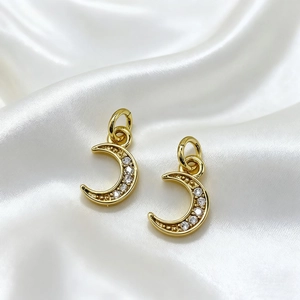 Macro detail of 18K gold plated crescent moon pendants with zircon micro-paving on silk