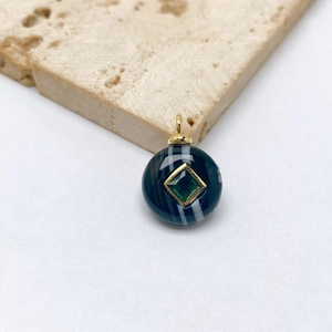 Macro shot of striped agate pendant with green gemstone inset on textured beige stone