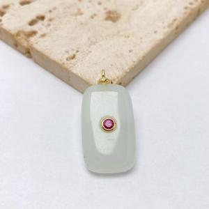 Macro detail of rectangle white stone pendant with pink gem and golden metal frame