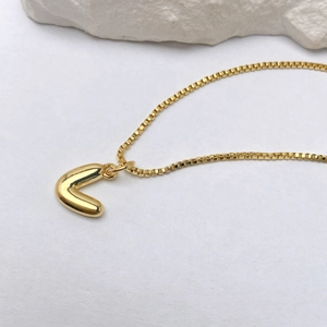 Detalle de un colgante de letra V en oro pulido con una elegante cadena de caja cuadrada