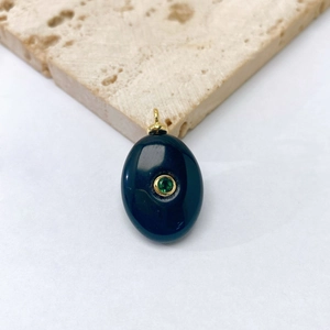 Macro shot of oval blue stone pendant with gold inlay and green gem detail