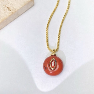 Macro detail of a gold chain with a circular reddish stone pendant and marquise gem