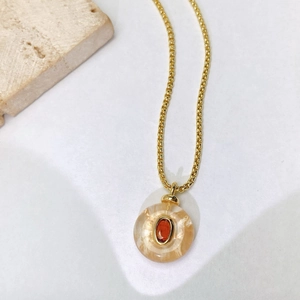 Macro detail of a golden necklace featuring a translucent amber-toned resin circular pendant