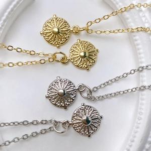 Macro detail of sunburst charm pendants in gold and silver finish with O-chains