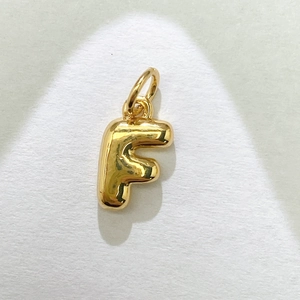 Detalle macro de un colgante de letra F burbuja 3D con acabado en oro pulido