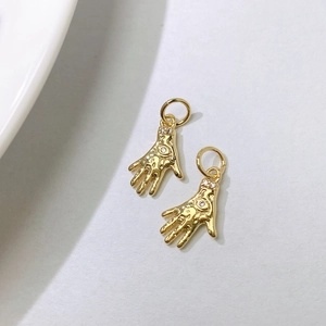 Macro shot of gold hand-shaped pendants with white zircons on textured white background