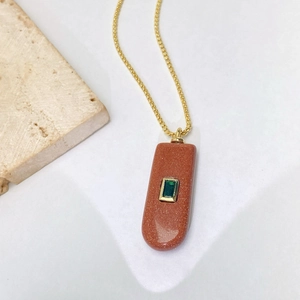 Vue détaillée du pendentif en pierre de soleil avec zircon vert et chaîne dorée