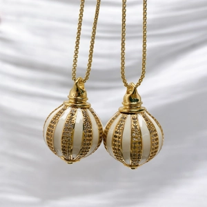 Detailed macro of golden sphere pendant with white enamel and sparkling zircon inlay