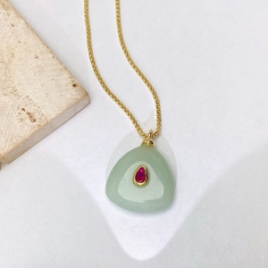 Détail d'un collier doré avec une pierre verte triangulaire et une gemme rouge goutte