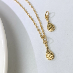 Detail of golden tennis racket pendant with textured mesh on a minimalist O-chain
