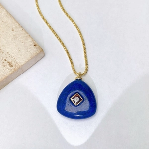 Détail d'un collier doré avec pendentif en pierre bleue triangulaire et incrustation de cristal