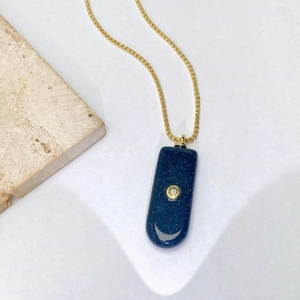 Détail d'une chaîne dorée avec pendentif rectangulaire bleu marine effet ciel étoilé