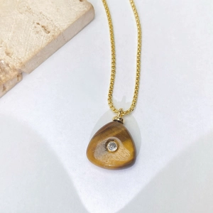 Gros plan d'un collier doré avec pendentif triangle en oeil de tigre et zircon