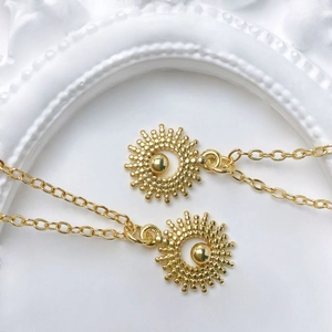 Detailed close-up of golden sunburst pendants with zircon on a fine link necklace chain