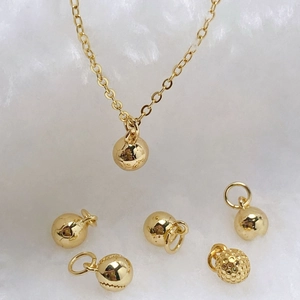 Elegant gold spherical pendant necklace set with various textured charms on soft white plush