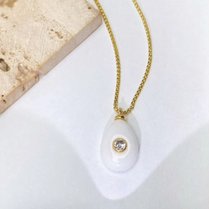 Détail du collier doré avec pendentif goutte blanc et zircon scintillant au centre
